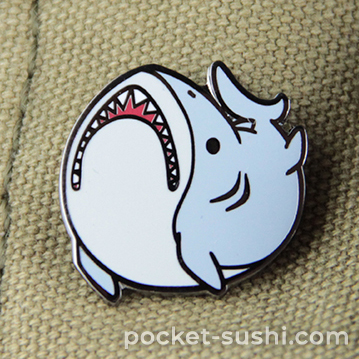 a photo of an enamel pin designed to look like a fat cartoon shark